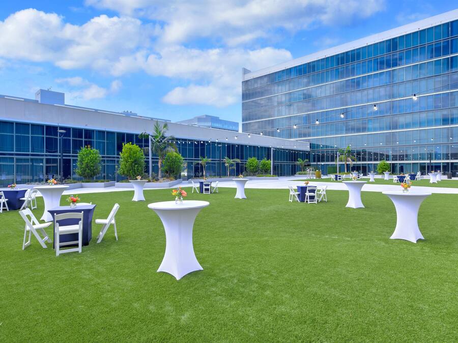 An outdoor event space with tables and chairs, a grassy lawn, and a modern building with large windows in the background.