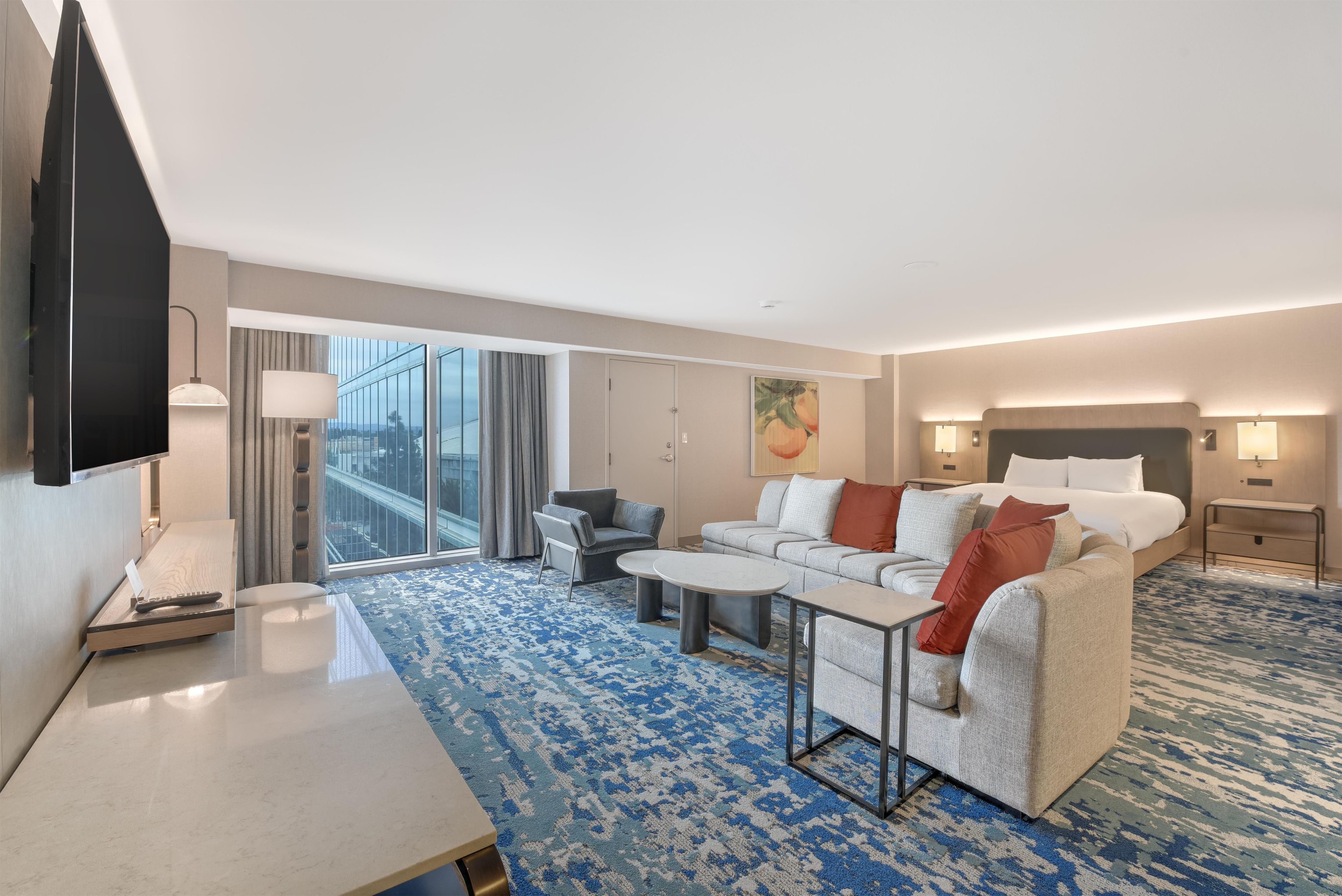 A modern hotel room with a large bed, a sofa, a coffee table, and a TV.