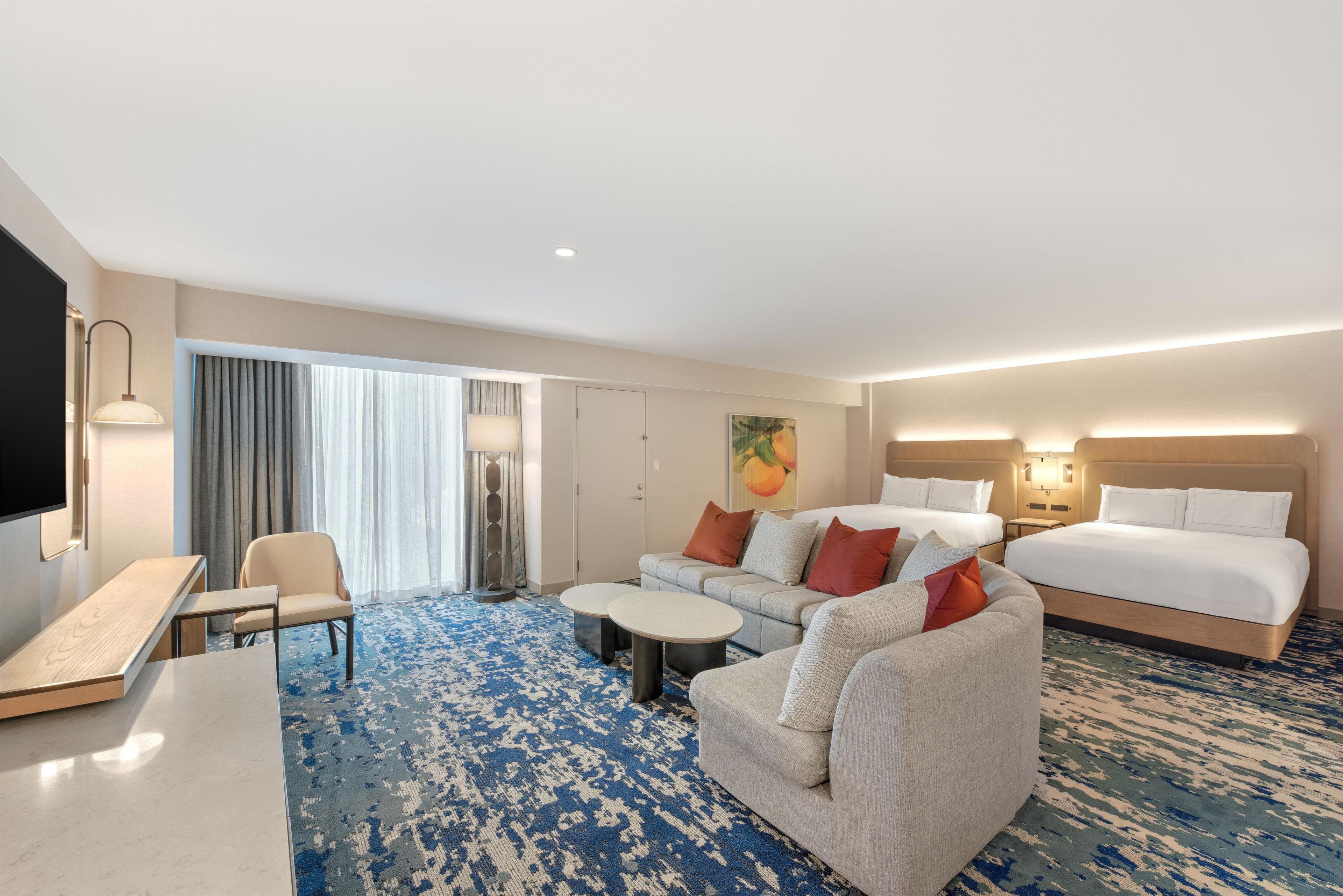 A hotel room with a sofa, two single beds, a desk, and a TV.