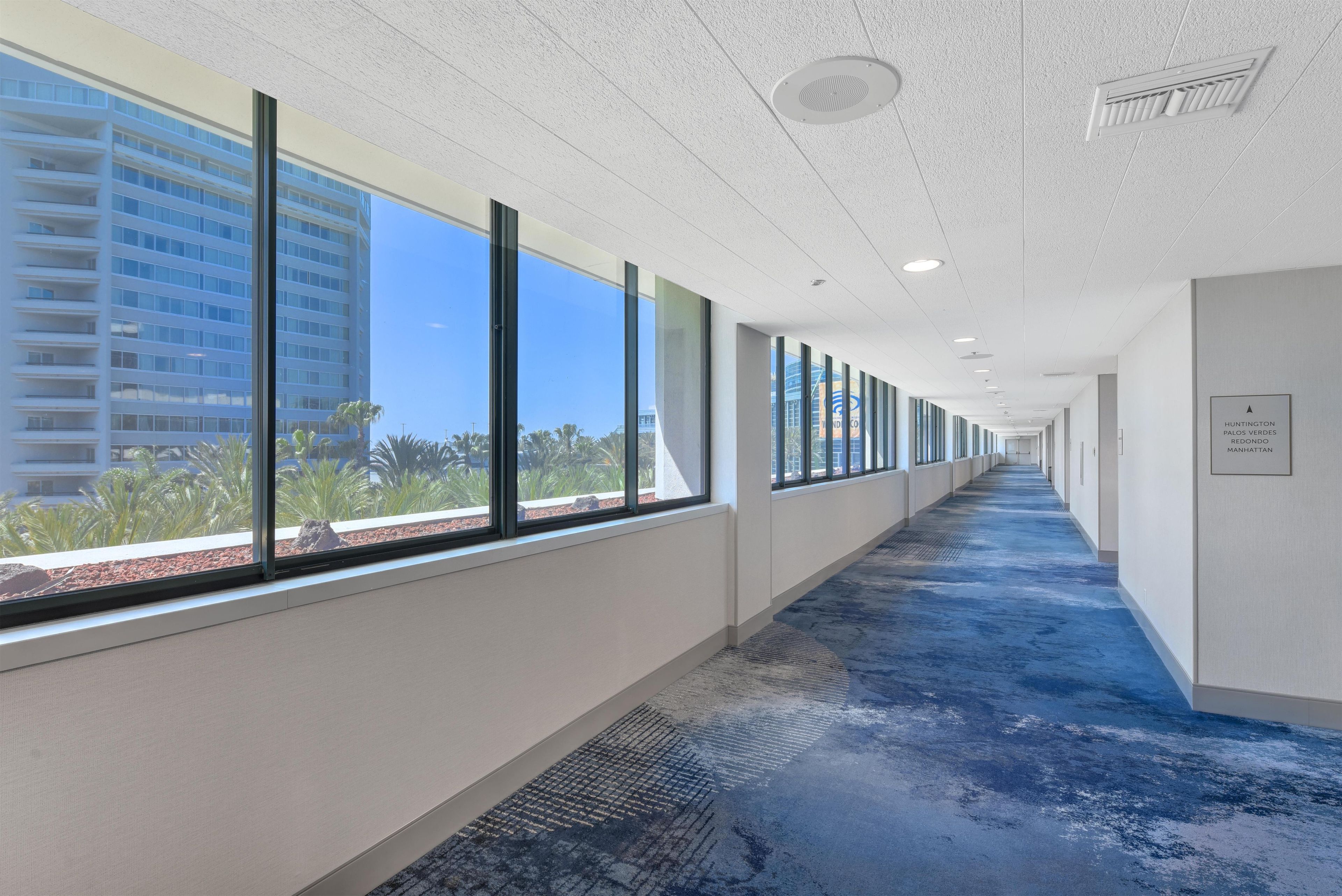 A corridor with large windows, a blue carpet, and a sign indicating the location.