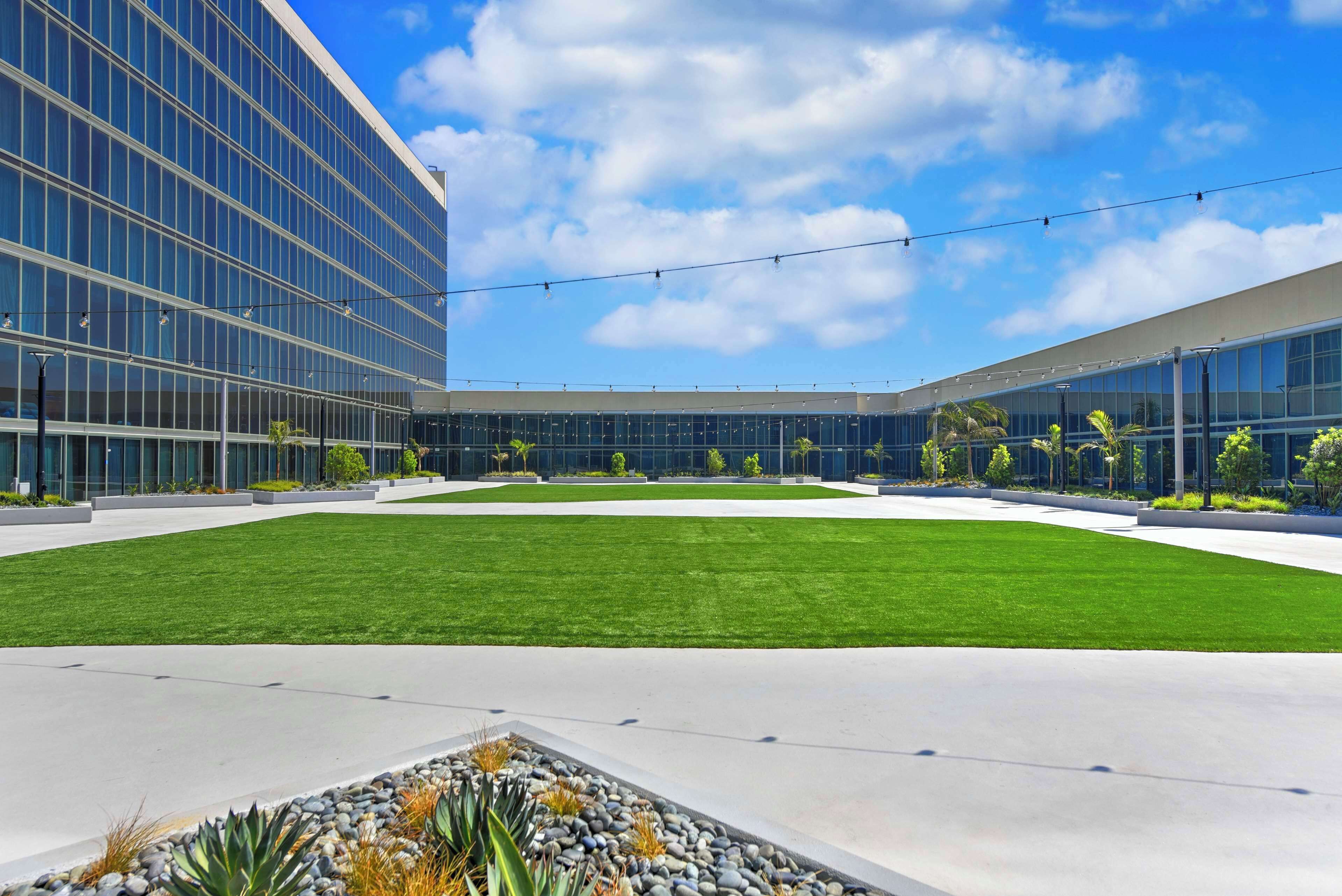 A modern building with a large glass facade, a central grassy courtyard, and a clear blue sky.