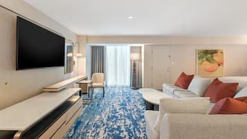 A hotel room with a flat-screen TV, a sofa, a coffee table, a chair, and a patterned carpet.