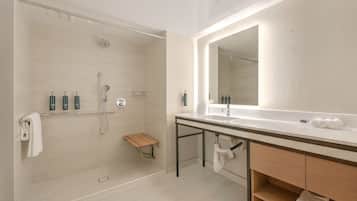 Un baño moderno con ducha a ras de suelo, un espejo grande y un tocador con lavamanos y toallero.
