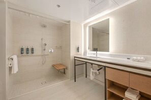 A modern bathroom with a walk-in shower, a large mirror, and a vanity with a sink and towel rack. - Hilton Anaheim (Anaheim)