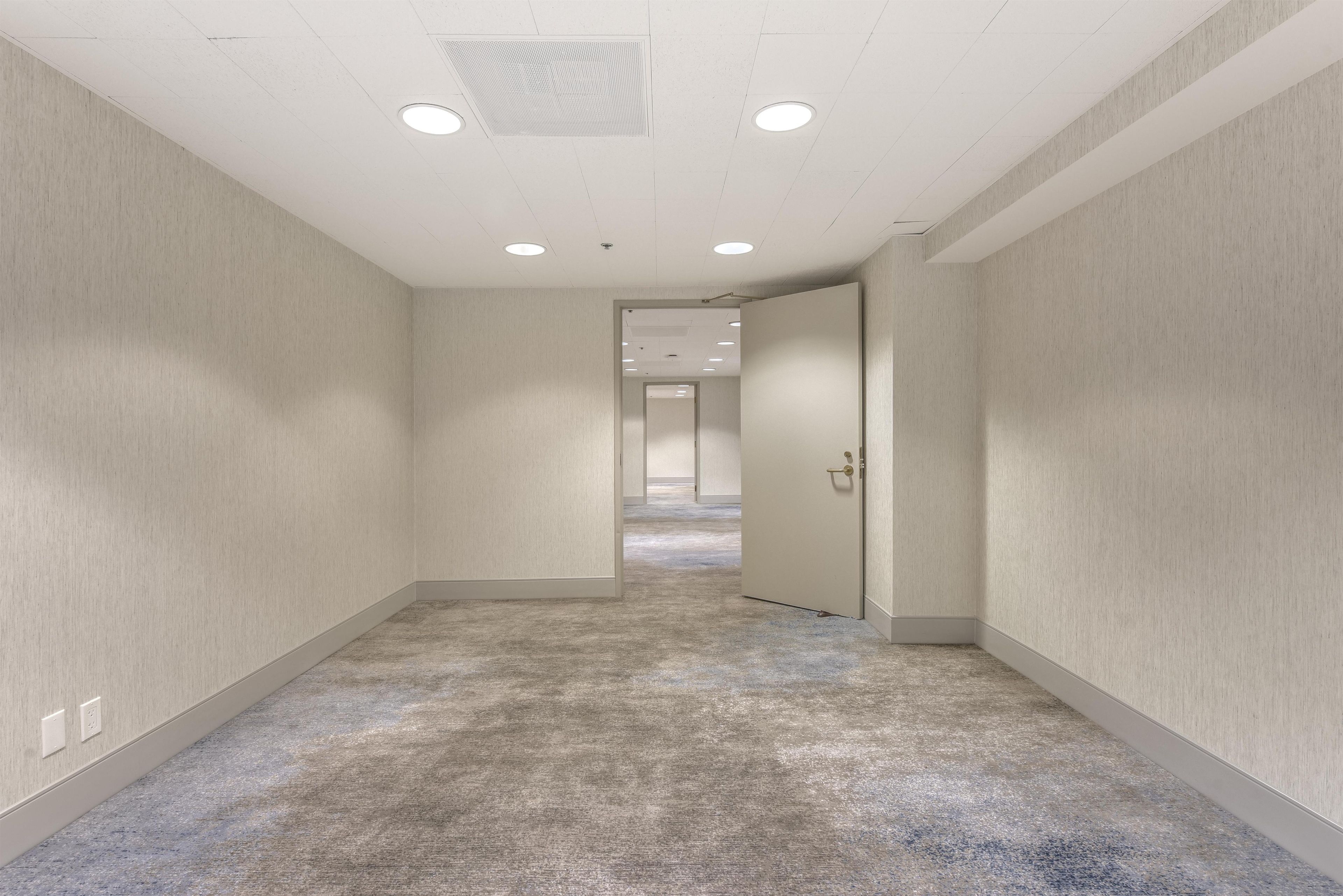 Un couloir doté de revêtements de sol en moquette, de murs blancs et de luminaires encastrés au plafond.