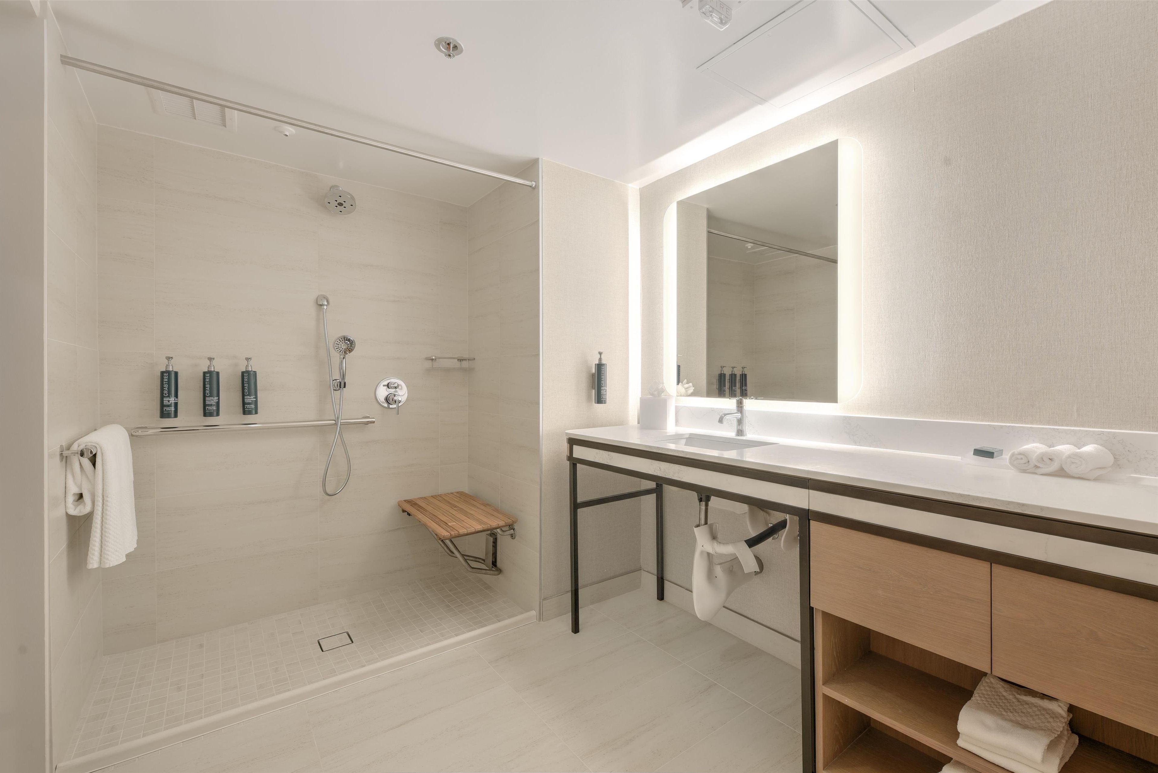 A modern bathroom with a glass-enclosed shower, a large mirror, and a wooden bench.