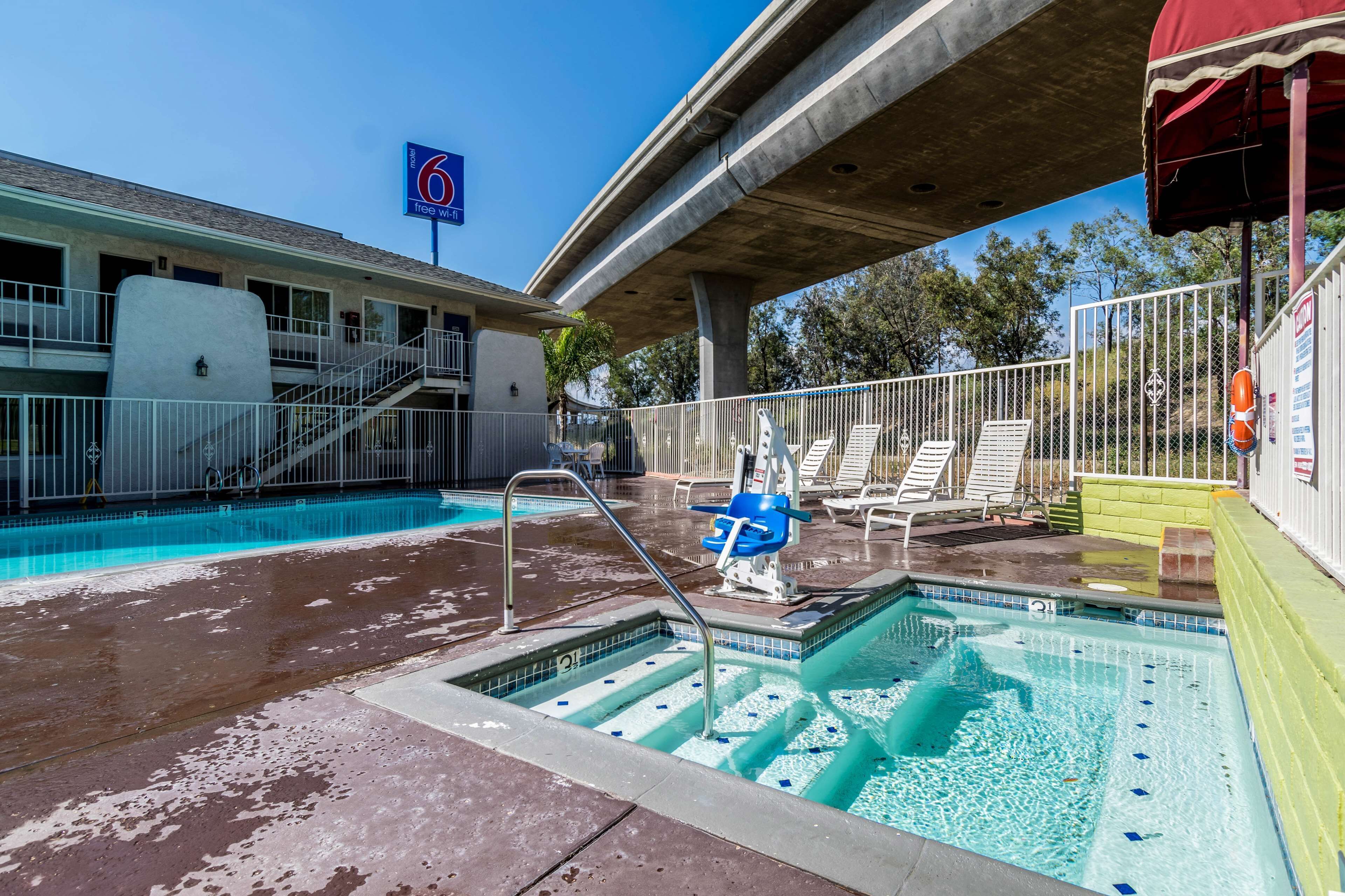 A hotel pool area with a lifeguard stand, lounge chairs, and a staircase leading to the building.
