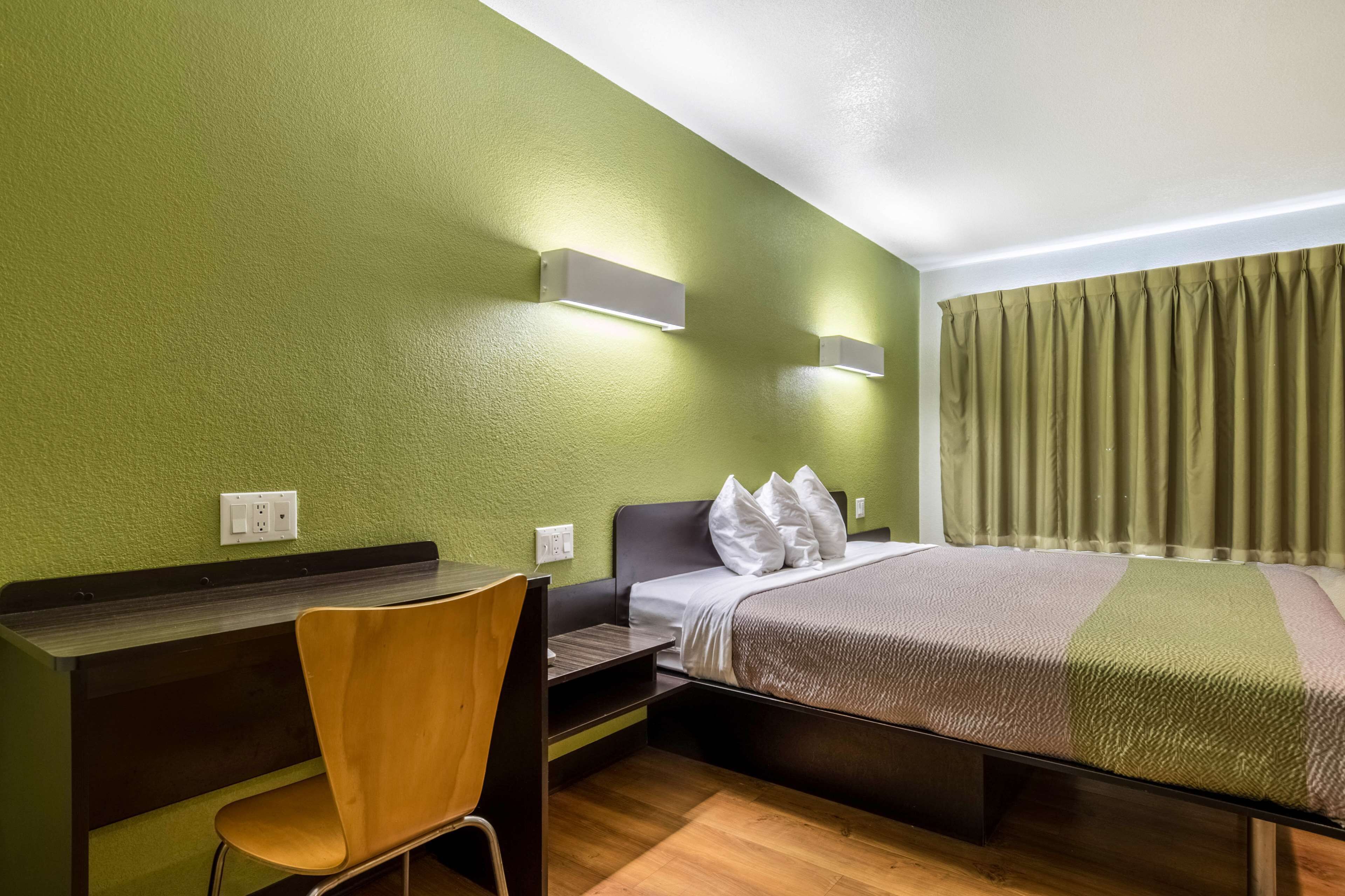 A hotel room with a bed, a desk, a chair, and a green wall.