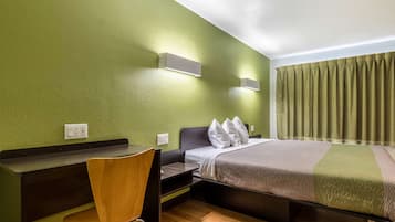 A hotel room with a bed, a desk, a chair, and a green wall.