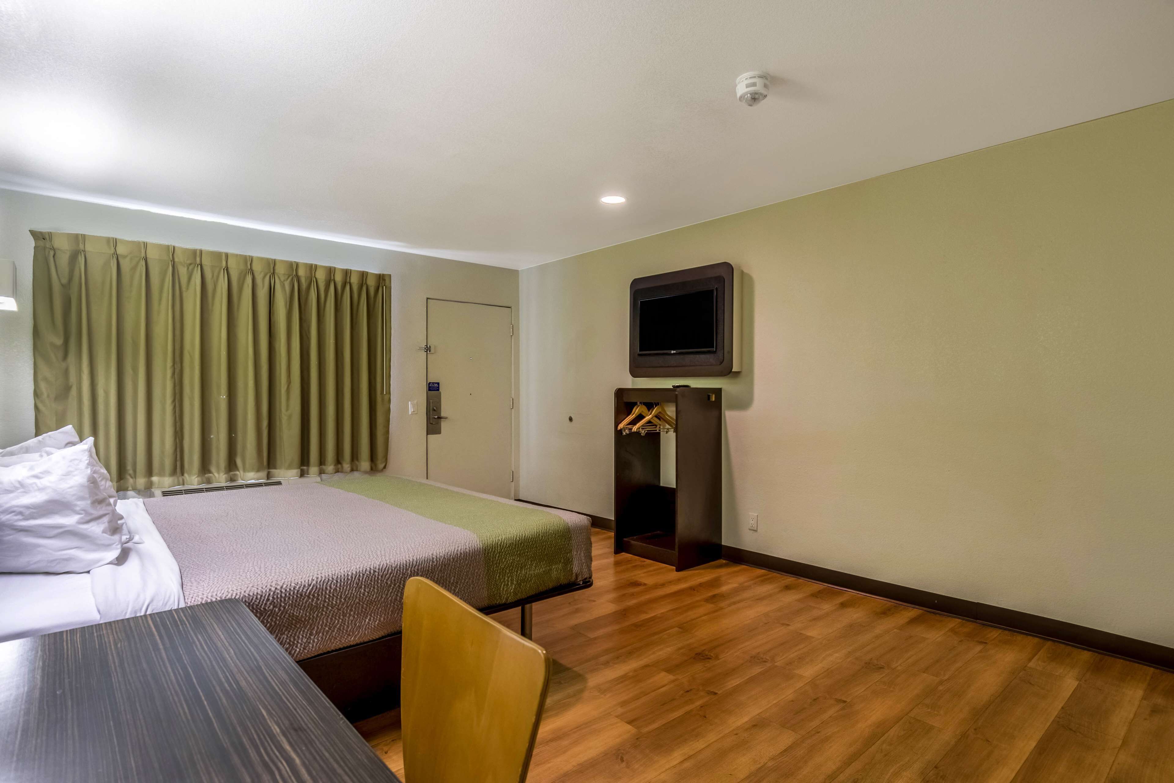 Une chambre d’hôtel équipée d’un lit, d’un bureau, d’une chaise, d’un téléviseur fixé au mur et d’un porte-manteau.