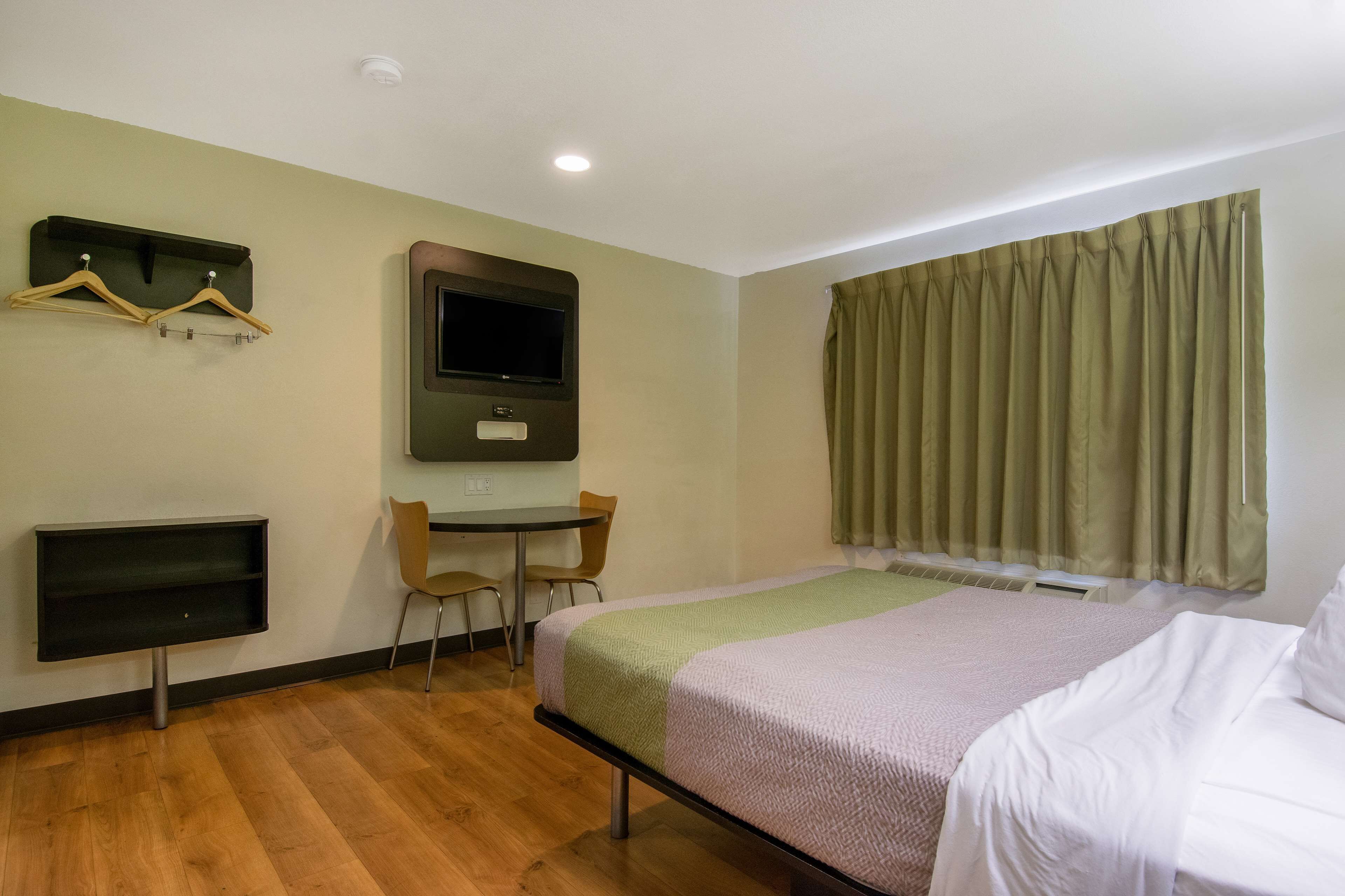 A hotel room with a bed, a desk, a chair, a TV, and a window with curtains.