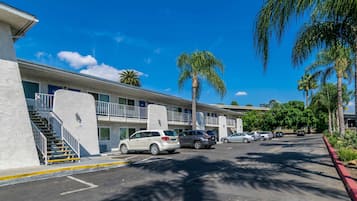 Un motel à plusieurs étages, doté d’un parking, de palmiers et surplombant un ciel bleu azur.