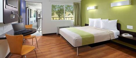 Habitación de hotel con una cama, un escritorio con una computadora portátil, una silla y una ventana con vistas al exterior.