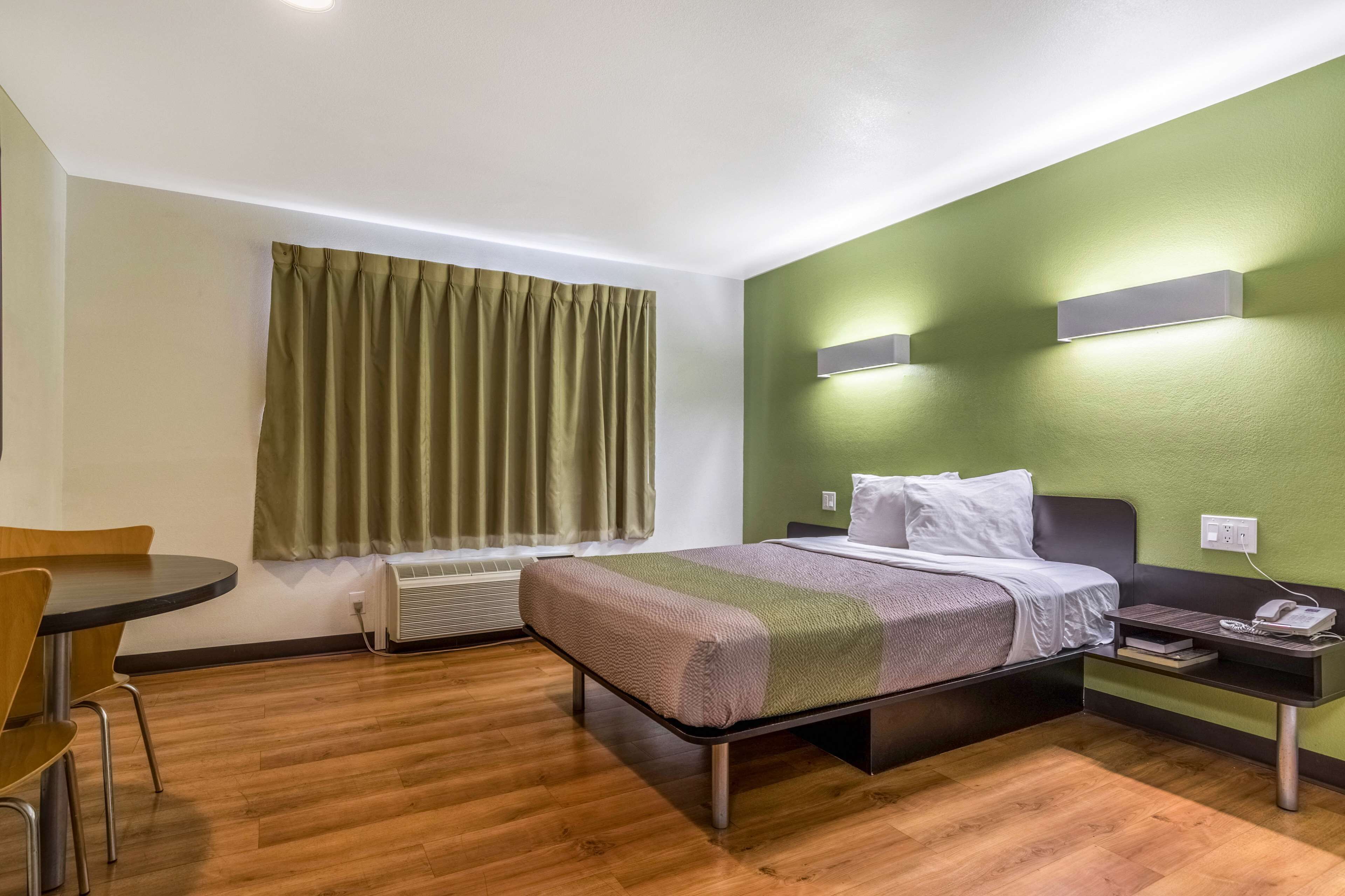 A hotel room with a bed, bedside table, chair, and a window with curtains.