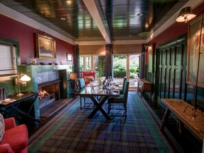 Enjoy dining in style with a central table and comfortable seating, flanked by a fireplace and large windows offering a view of the outdoors.