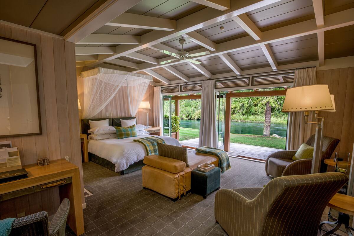 Un dormitorio con cama, mesita de noche, silla y vista al río.