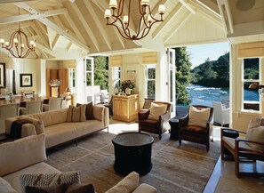 Relax in a spacious room with a sofa, armchairs, and dining table, offering a view of the river and surrounding greenery.