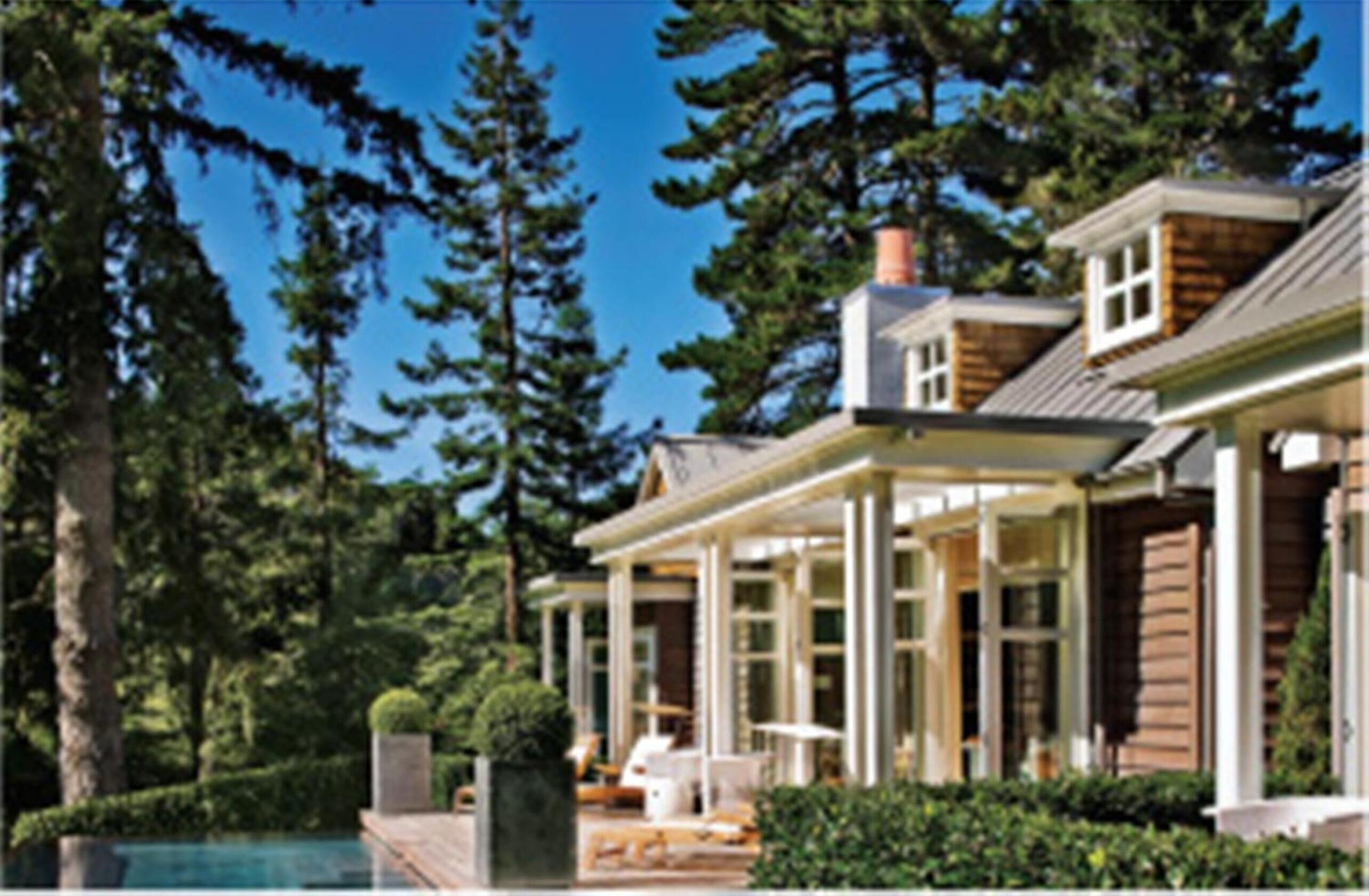 A modern house with a covered patio, a swimming pool, and a forested backdrop.