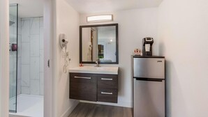 A modern bathroom with a glass shower enclosure, a dark wood vanity with a mirror, and a built-in refrigerator. - Revival Scottsdale Studios (Scottsdale)
