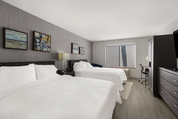 A hotel room with two beds, a desk, a chair, a TV, and artwork on the wall.