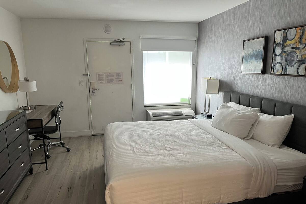 A hotel room with a bed, a desk, a dresser, and a window with blinds.