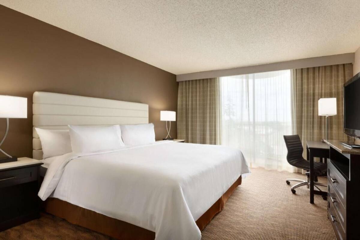 Ein Hotelzimmer mit einem großen Bett, zwei Nachttischlampen, einem Schreibtisch mit Stuhl und einem Fernseher.