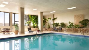 Una piscina interior con agua azul cristalina, rodeada de sillones de descanso y plantas en macetas.