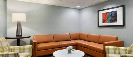Eine Sitzecke mit einer braunen Ledersofa, zwei karierten Sesseln, einem kleinen runden Tisch mit einer Vase und einem gerahmten abstrakten Gemälde an der Wand.