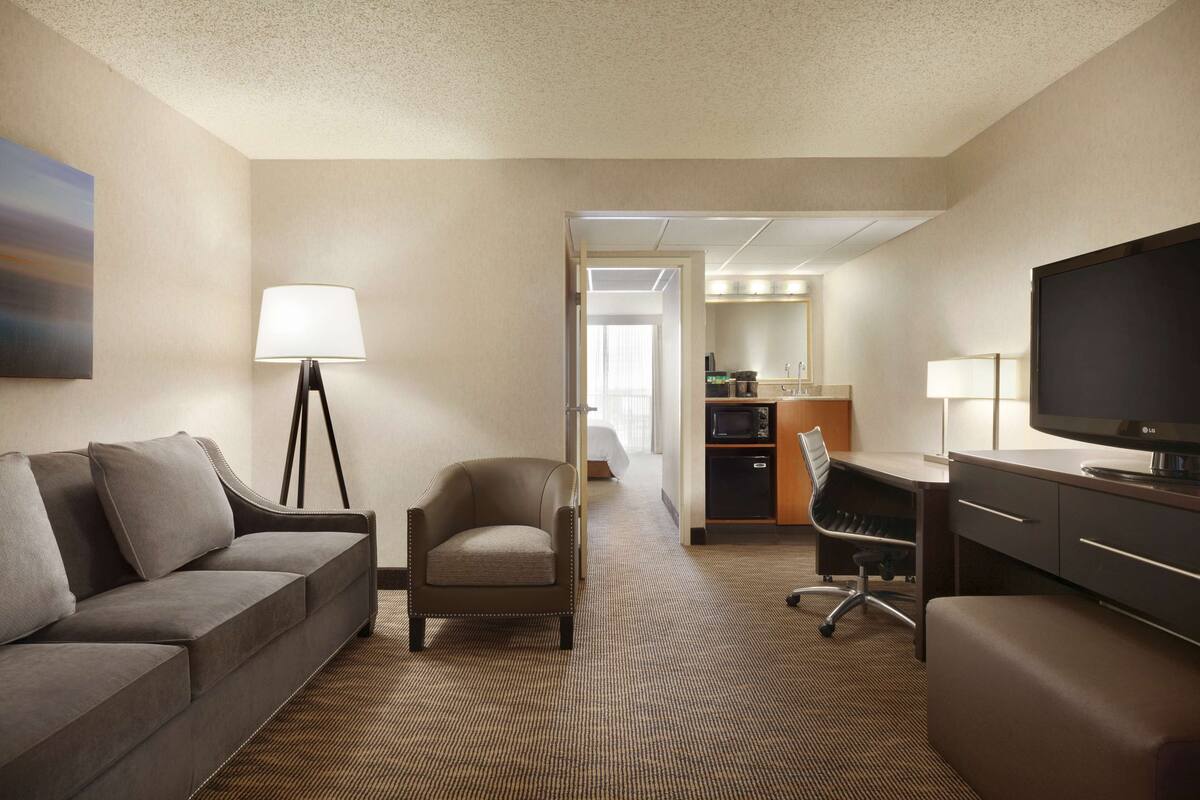 Ein Hotelzimmer mit Sofa, Sessel, Schreibtisch, Fernseher und einer Küchenzeile.