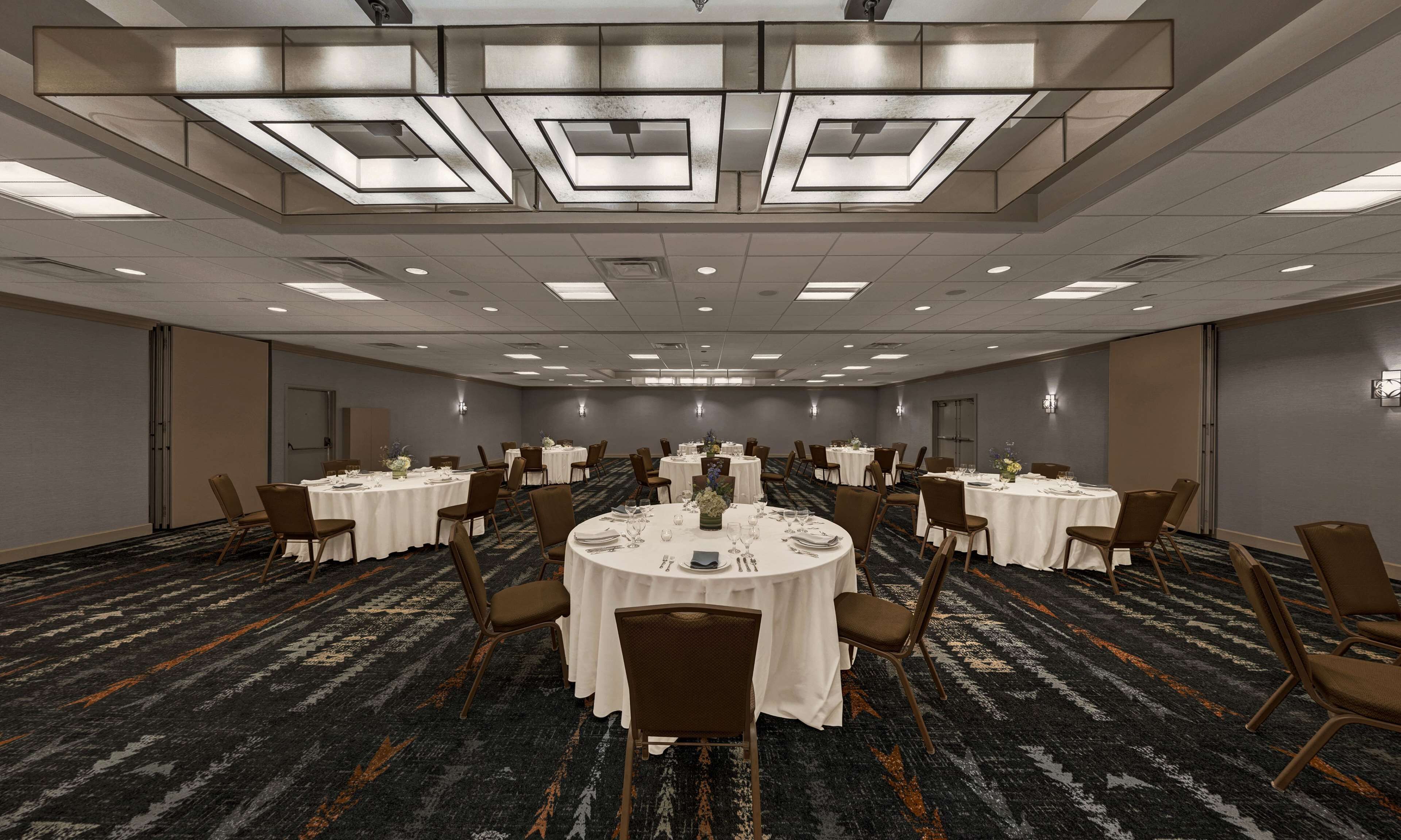Un salón de conferencias con mesas redondas, sillas y suelo alfombrado.