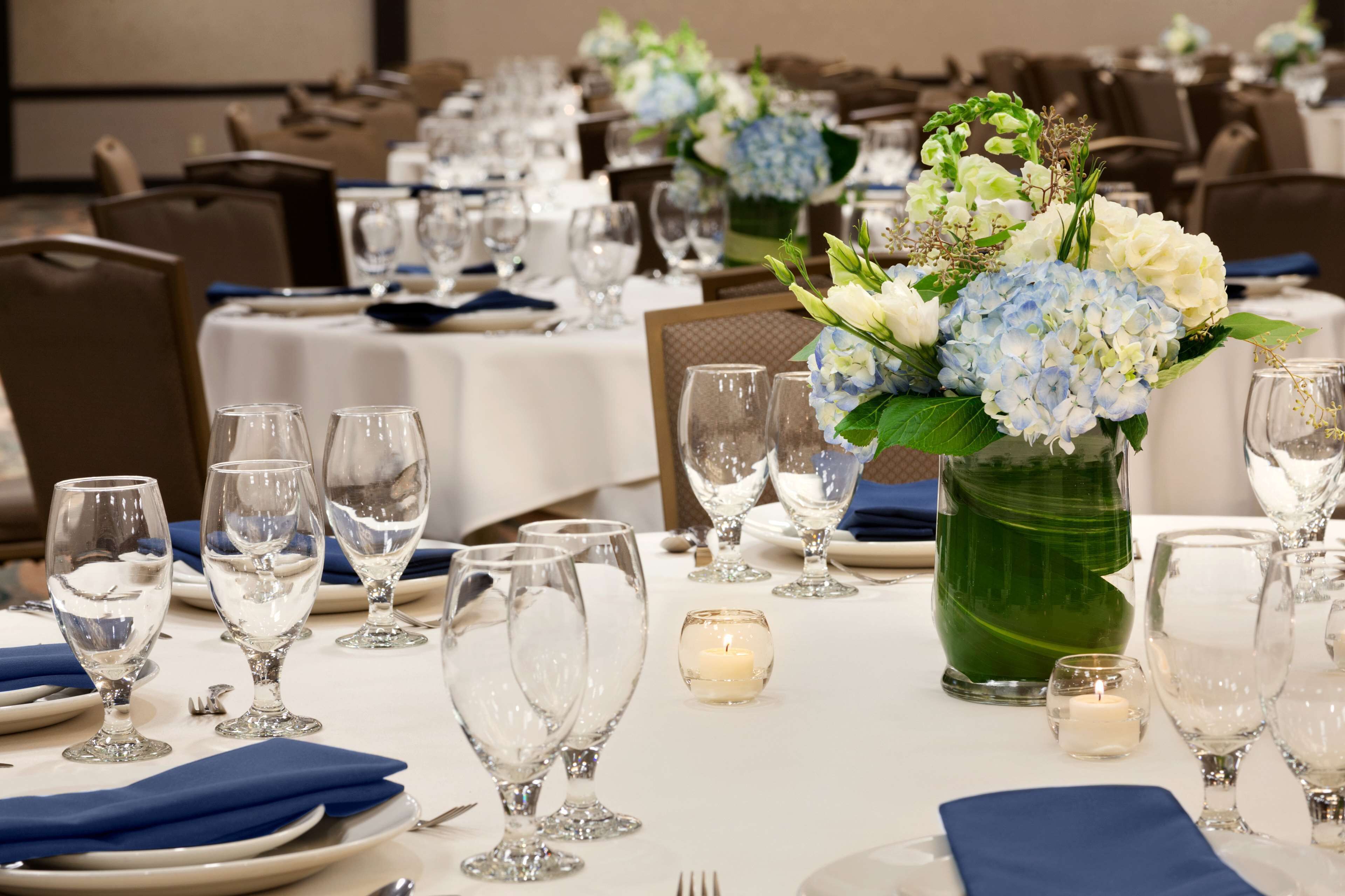 Un salón de banquetes con mesas dispuestas para un evento formal, con centros de mesa florales y candelabros.