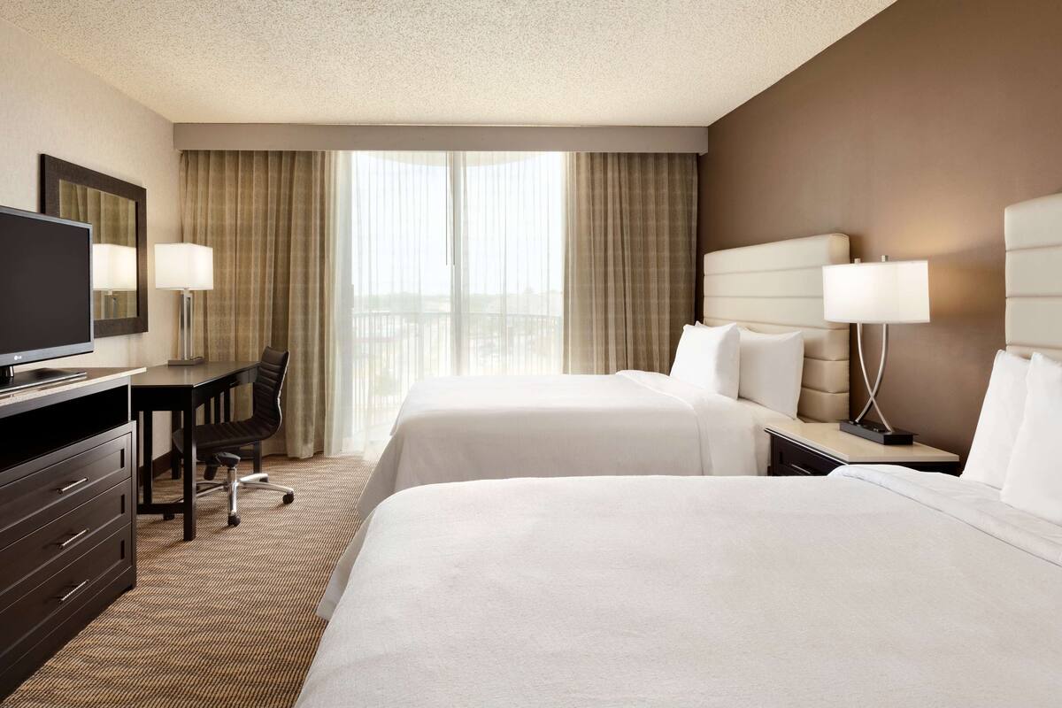 Ein Hotelzimmer mit zwei Betten, einem Schreibtisch, einem Fernseher und Blick ins Freie.
