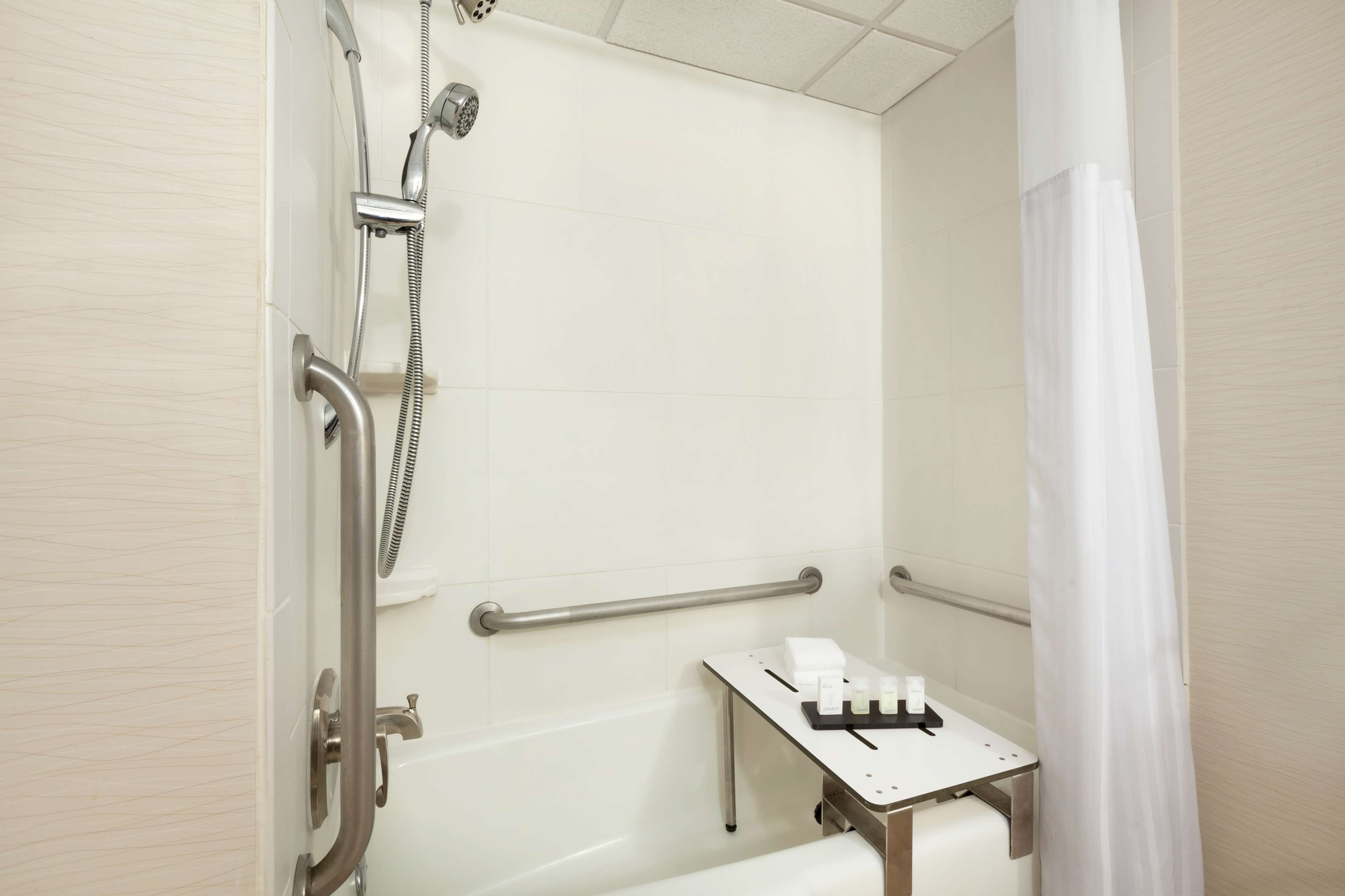 Une salle de bain équipée d’une douche, de barres d’appui et d’une petite table sur laquelle sont posés les articles de toilette.