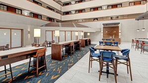 Un vestíbulo de hotel de varios niveles con una escalera central, varias áreas de comedor y un bar.