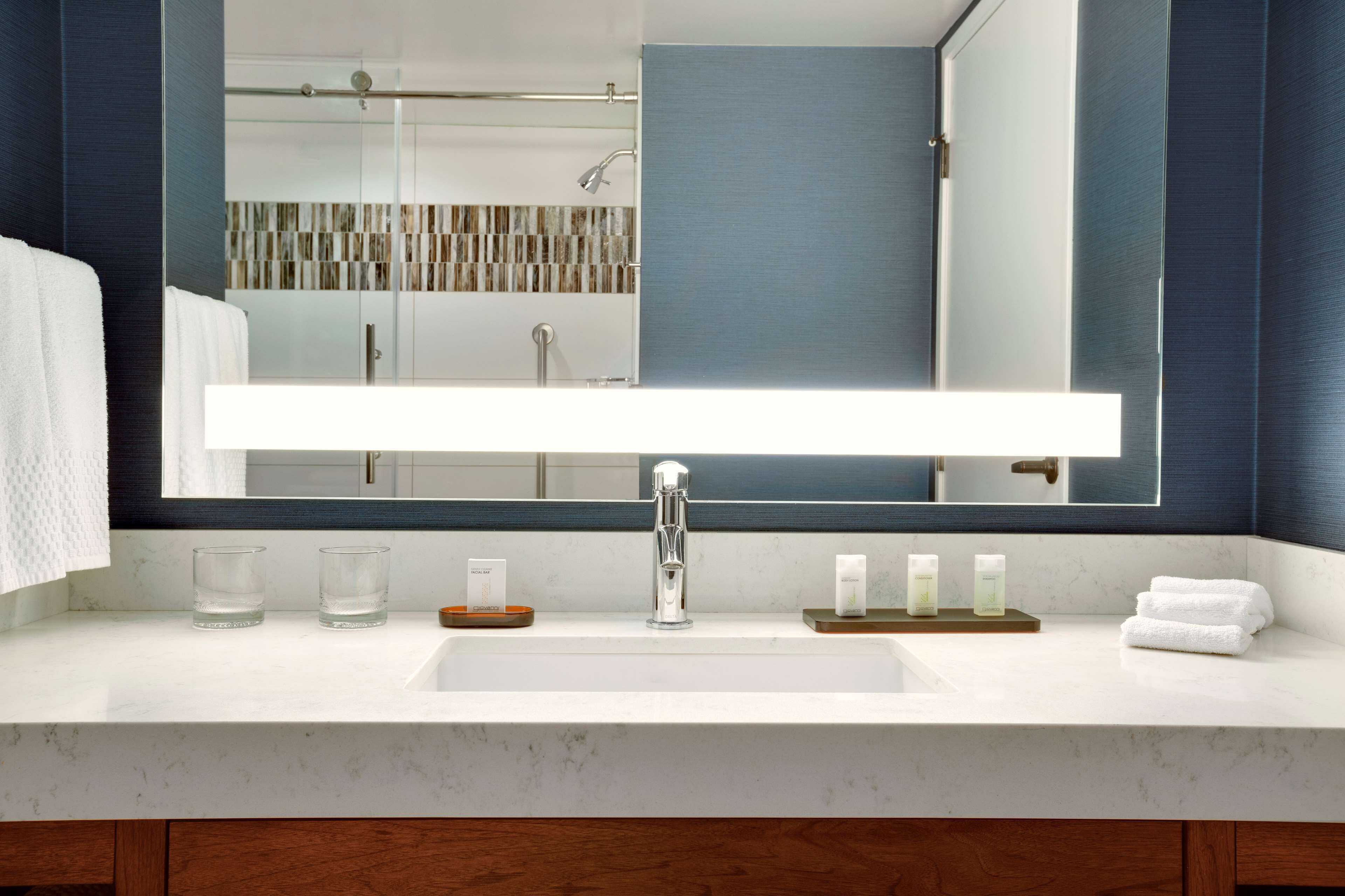 Un baño moderno con un espejo grande, lavamanos blanco y cabina de ducha de vidrio.