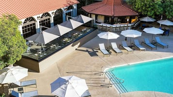 A rooftop pool area with lounge chairs and umbrellas, a bar, and a building with a red-tiled roof.