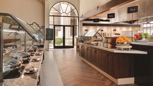 A buffet area with a variety of food stations, including a bakery and fruit section, and a view of the outdoor area through an arched doorway. - Embassy Suites by Hilton Scottsdale Resort (Scottsdale)