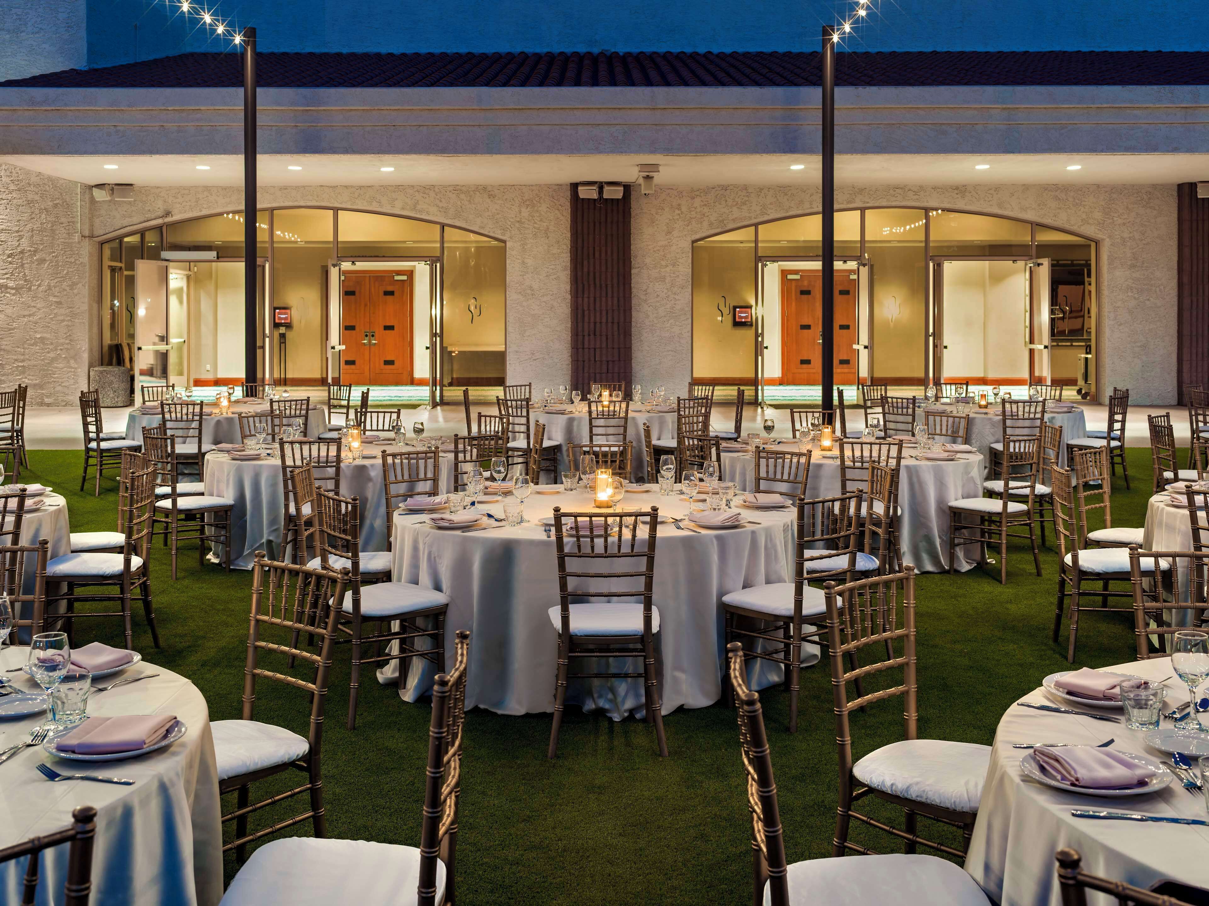 Un espacio comedor exterior formal con mesas redondas, sillas y velas.