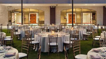 Un espacio comedor exterior formal con mesas redondas, sillas y velas.