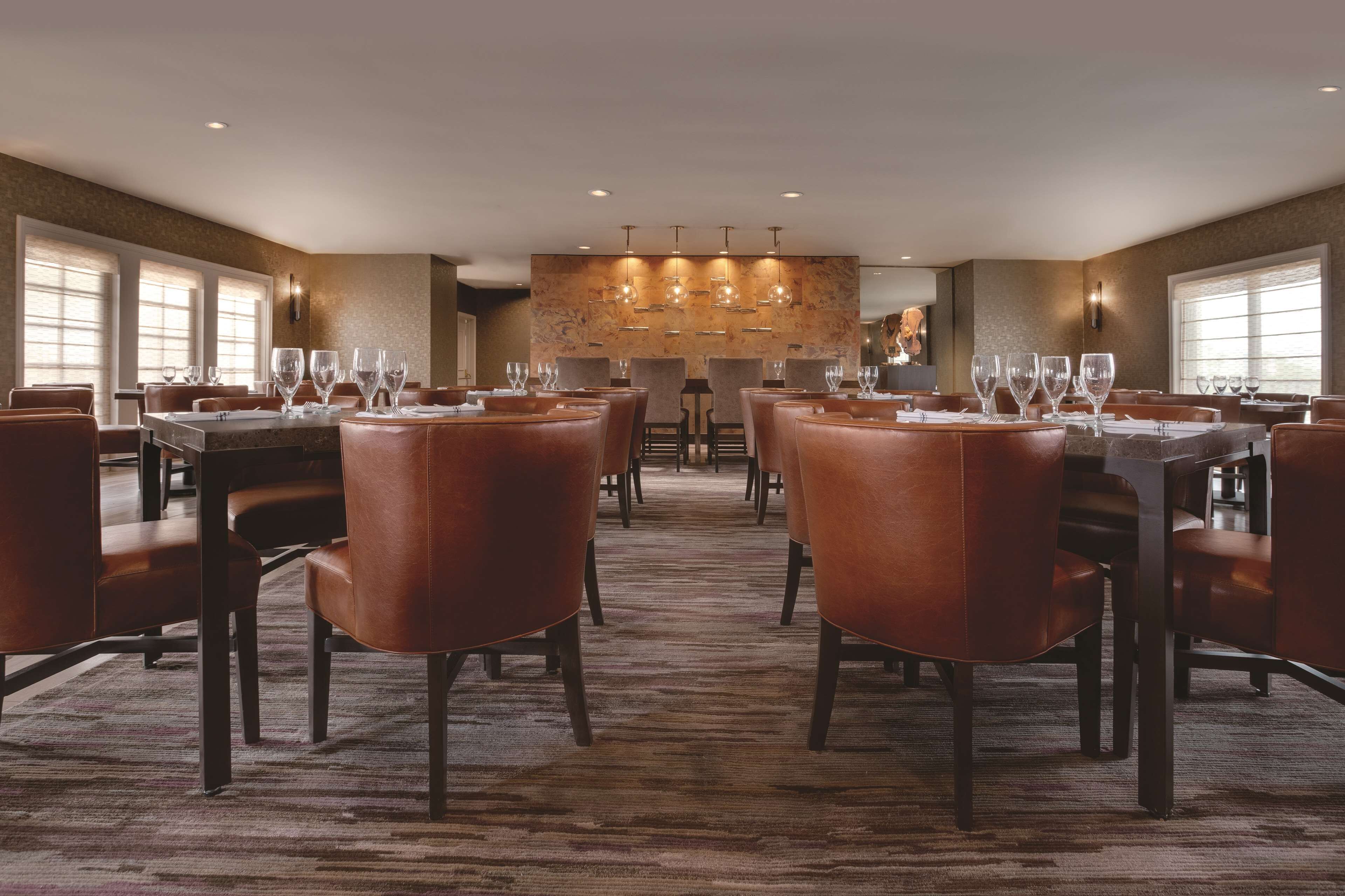 A spacious dining area with multiple tables and chairs, large windows, and a central chandelier.