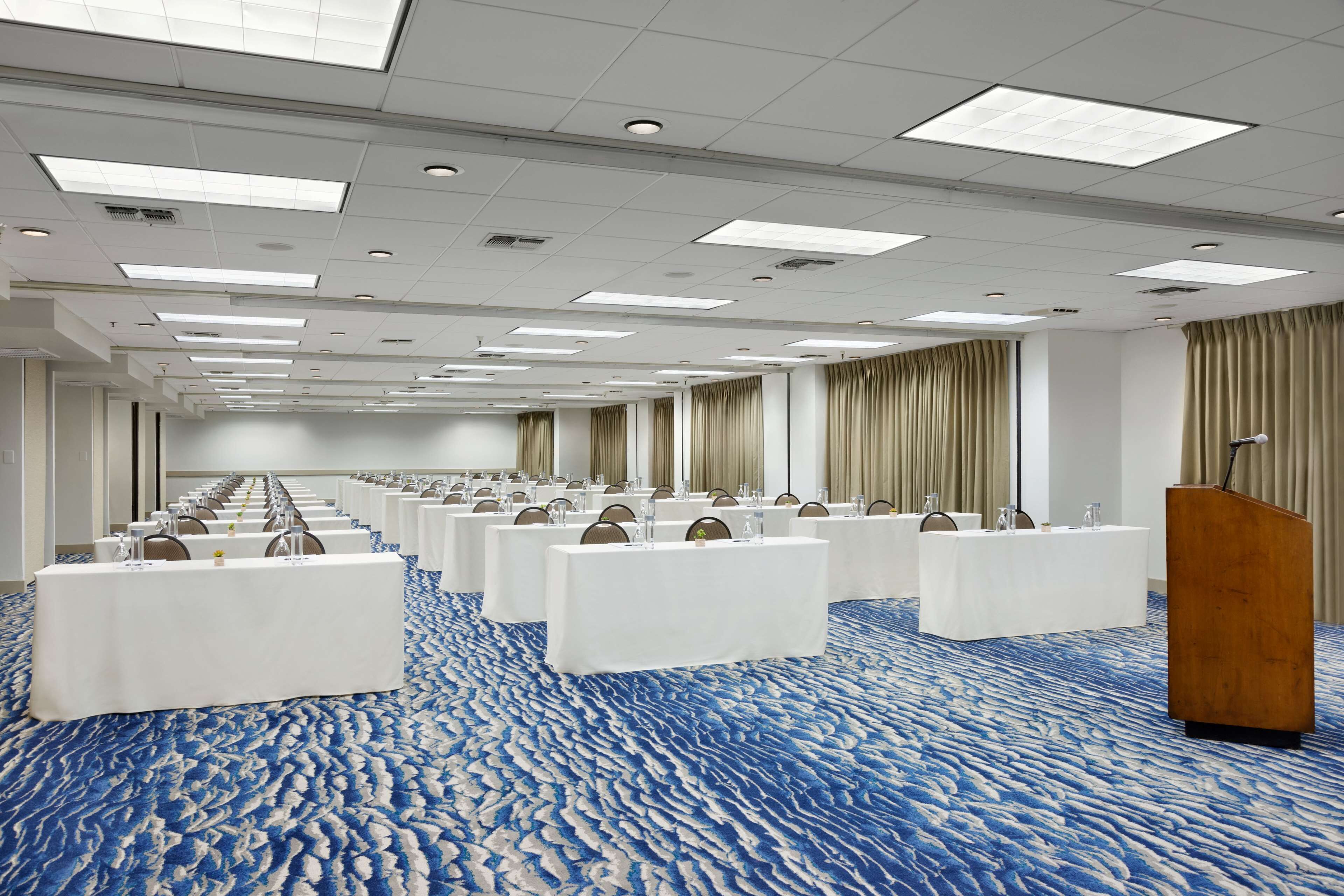 Un salón de conferencias con filas de mesas y sillas, un atril y una alfombra estampada.