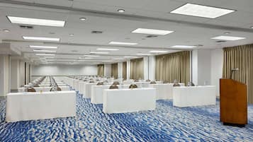 A conference room with rows of tables and chairs, a podium, and a patterned carpet.