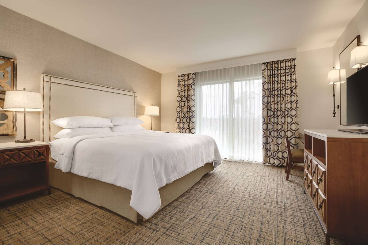 A hotel room with a large bed, a wooden nightstand, a dresser, and a television.