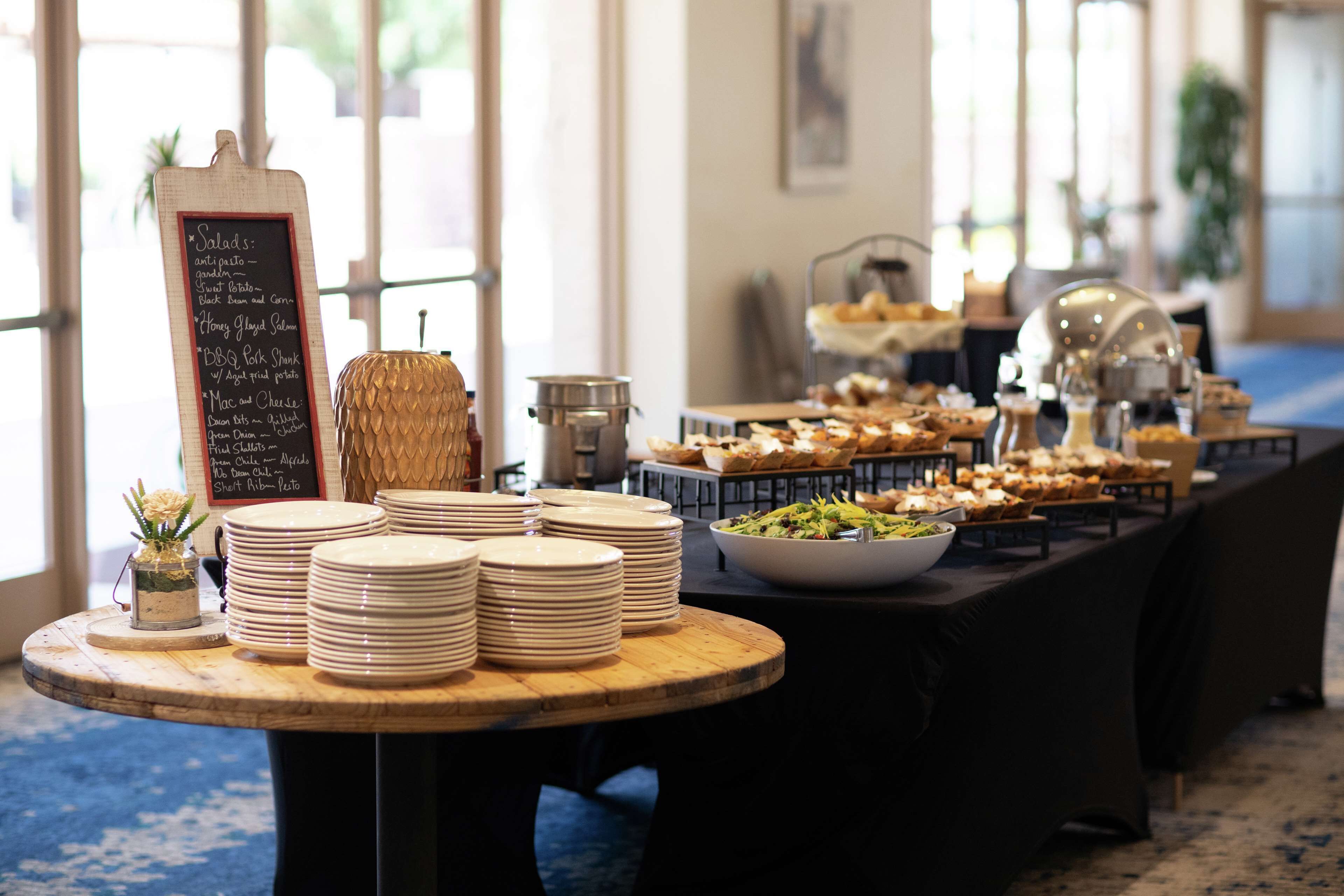 A buffet setup with various dishes and a chalkboard menu listing items like salads, pasta, and desserts.