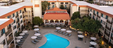 A hotel with a central swimming pool, outdoor seating, and a view of the surrounding cityscape.