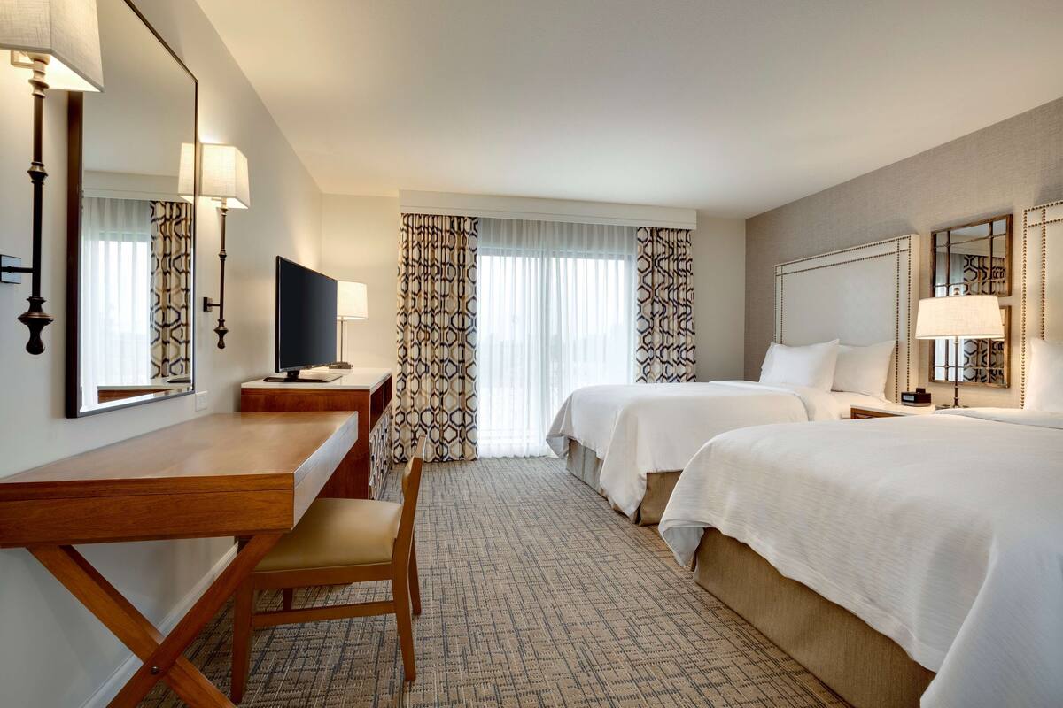 A hotel room with a wooden desk, two beds, a TV, and patterned curtains.