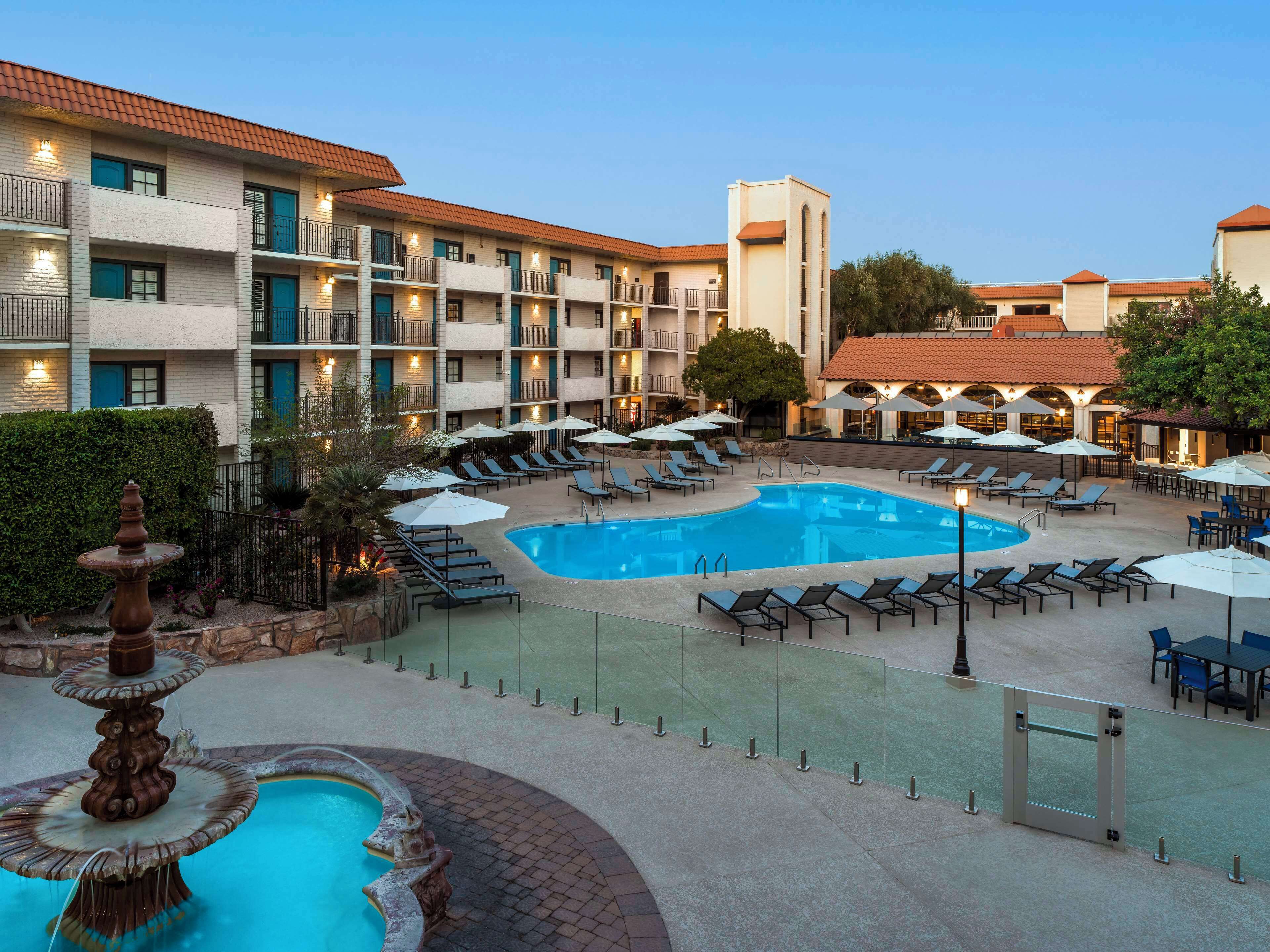 Um hotel com piscina, espreguiçadeiras e uma fonte.