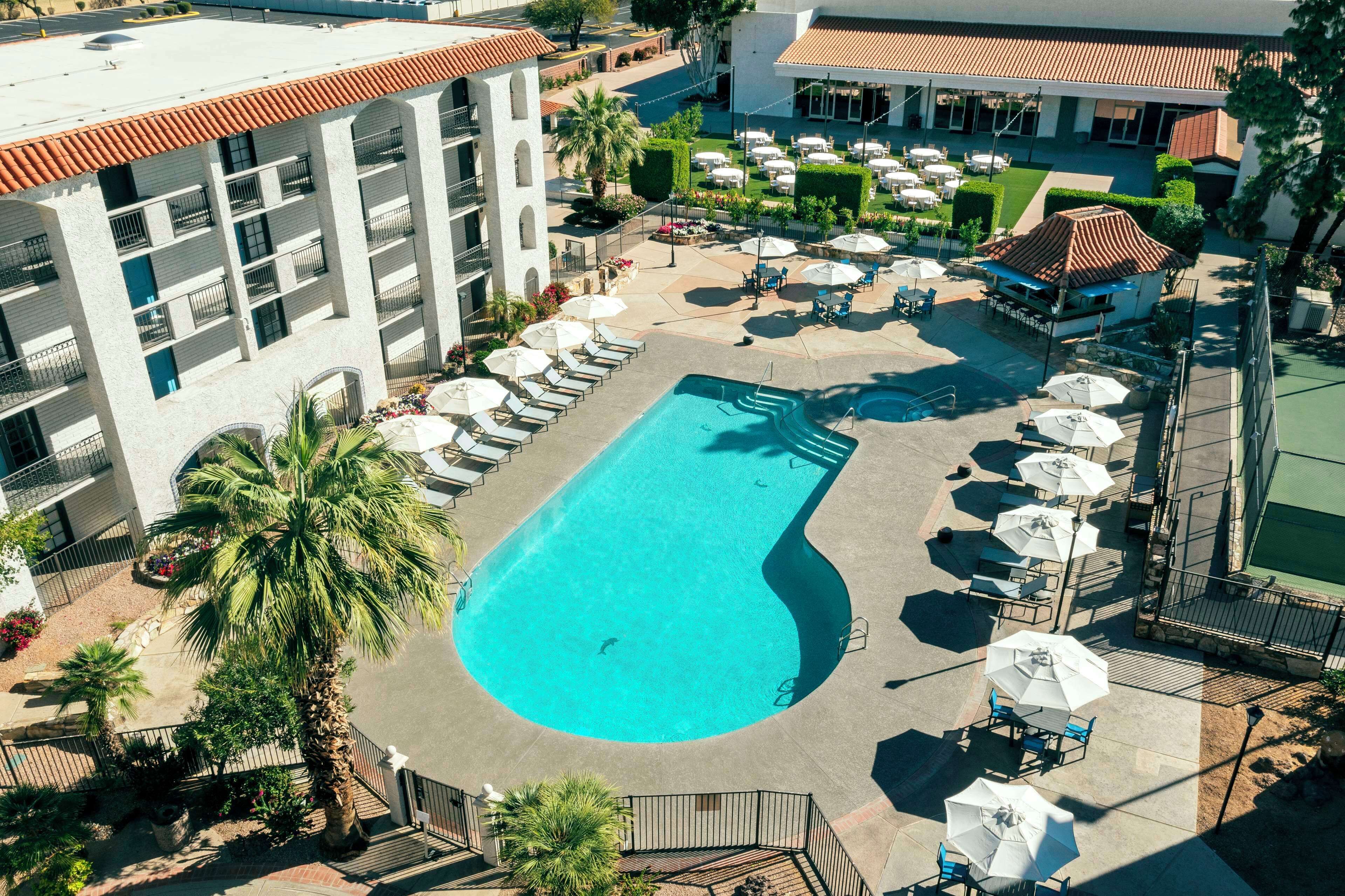 Un espace piscine aménagé sur le toit, avec des chaises longues et des parasols, entouré d’un bâtiment doté de balcons et d’un toit recouvert de tuiles.