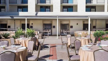 An outdoor dining area with tables and chairs, a stone wall, and a building with balconies in the background.