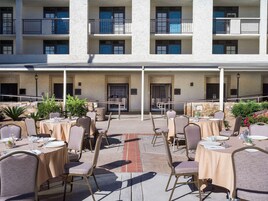 An outdoor dining area with tables and chairs, a stone wall, and a building with balconies in the background.